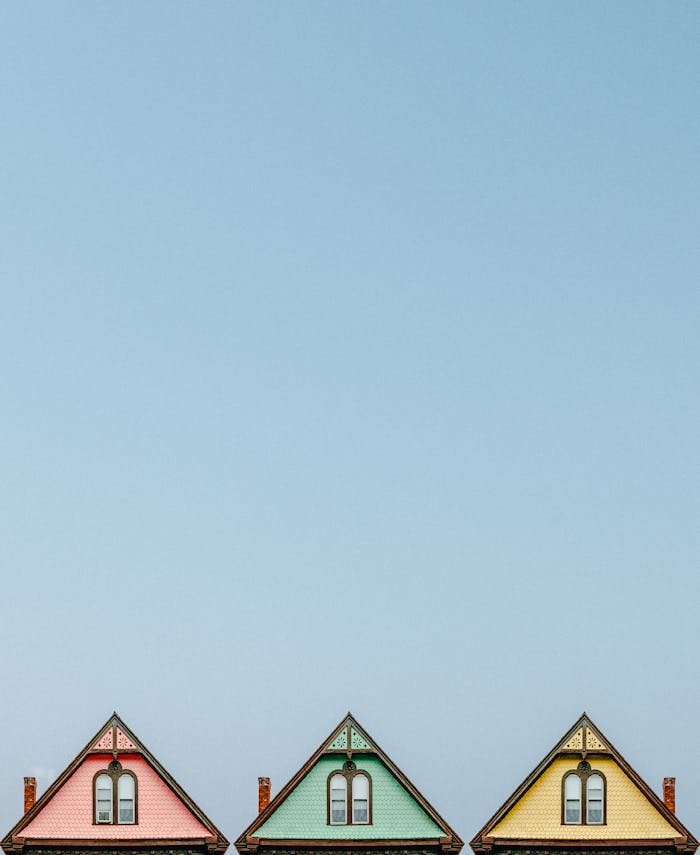 Three colorful triangular rooftops against a clear blue sky, showcasing simple architectural design.